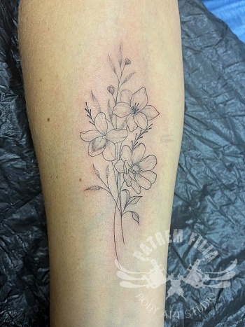 Delicate fine line bloemenboeket tattoo op onderarm