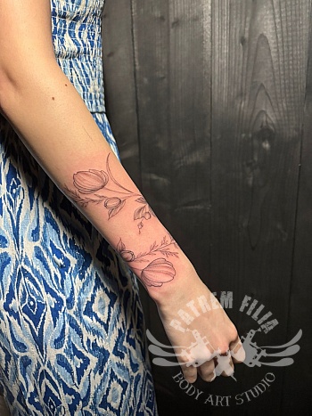 Fijne botanische armband tattoo met bloemen op de onderarm