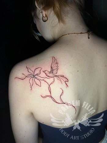 Fine line tattoo van een vogel met lelie op het schouderblad
