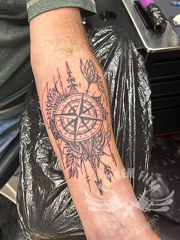 Geometrische kompas tattoo met natuurlijke details op onderarm