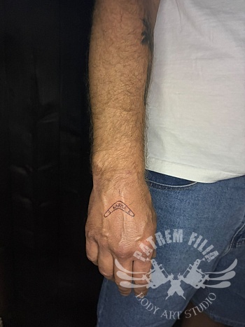 Minimalistische boomerang tattoo met tekst op de hand