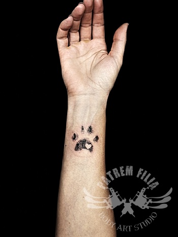 Minimalistische pootafdruk tattoo met inkt effect op de pols