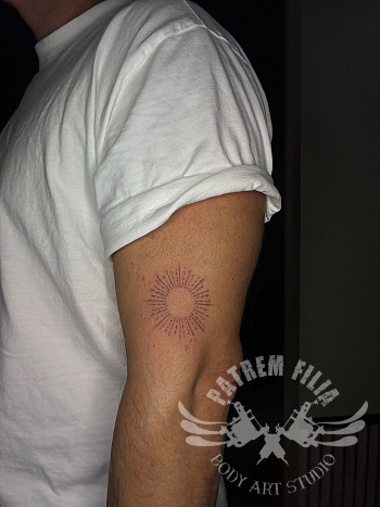 Minimalistische sunburst tattoo op de bovenarm