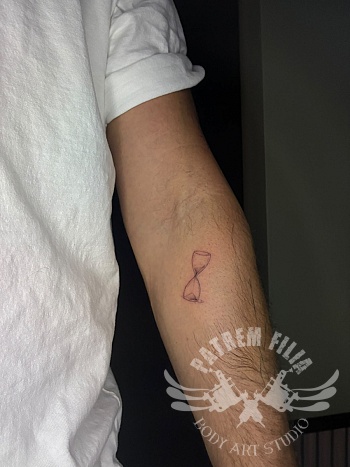 Minimalistische zandloper fine line tattoo op onderarm