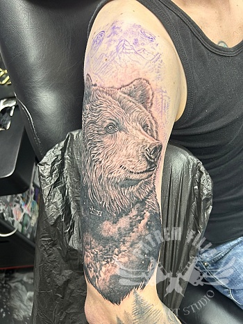 Realistische berenportret tattoo met boslandschap op bovenarm