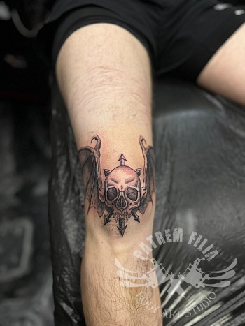 Skull tattoo met vleugels en Chaos symbool op de knie