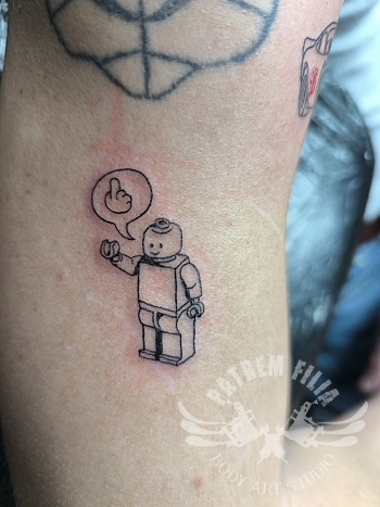 Speelse LEGO figuur tattoo met quote op de arm